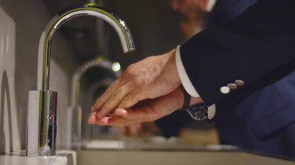 Close up of businessman washing hands in sink in public restroom