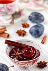 Delicious homemade plum jam with cinnamon and star anise on a white wooden background. Fresh fruit, spices and cups of tea on the table. Selective focus