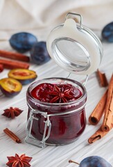 Jar with homemade plum jam with cinnamon and star anise on a white wooden background. Fresh fruit...
