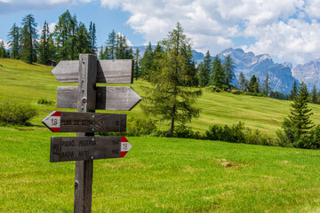Alpine crossroad with signs indicating to hikers directions and distances to world famous peaks and huts surrounded by green meadows. Val Badia, South Tyrol - Italy