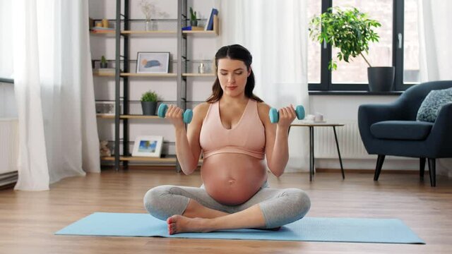 sport, fitness and pregnancy concept - happy pregnant woman with light dumbbells exercising at home