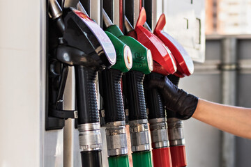 A woman's gloved hand reaches for a gasoline pump pistol at a gas station. Refueling the car