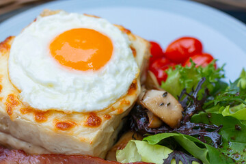 Croque madame delicious breakfast with ham, cheese, egg and spinach with vegetables. Cut fried egg on Croque madame, ham and cheese closeup on the plate. Eating croque-madame with beautiful fried egg.