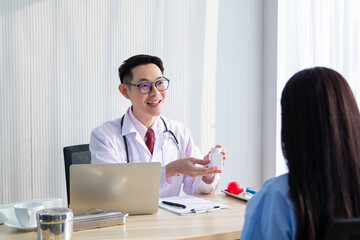 Fototapeta premium Young doctor showing a bottle of pills to the patient. Doctor describing new pills in pill-bottle to his female patient. Young male doctor prescribed medication to the female patient.