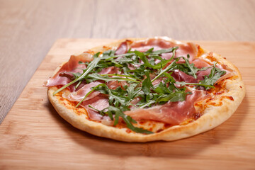Pizza with prosciutto, cheese and arugula on wooden board
