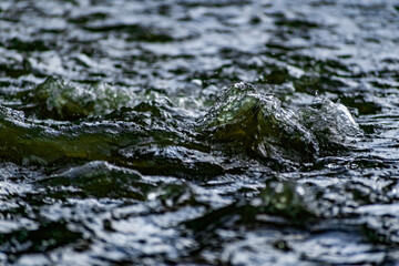 Fresh water in motion, swirling current with flying spray. Green tint on the light, transparent liquid in the river, like small waves for background and texture