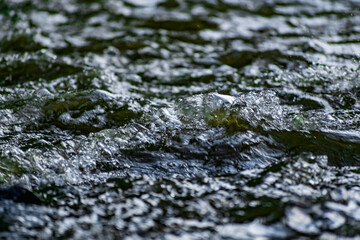 Fresh water in motion, swirling current with flying spray. Green tint on the light, transparent liquid in the river, like small waves for background and texture