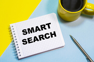SMART SEARCH on a notepad on a blue-yellow background, a cup of coffee and a pen. Business concept