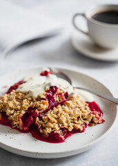 Plum crumble on white plate with coffee close up. Autumn and winter comfort food, cosy atmosphere, nordic style