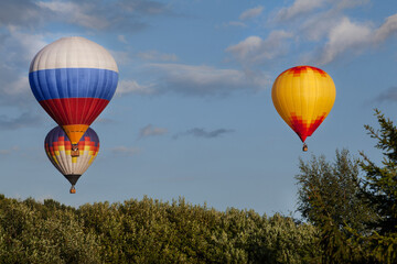 Three multi-colored hot air balloons with tourists flying over the summer forest. Some clouds in the sky.