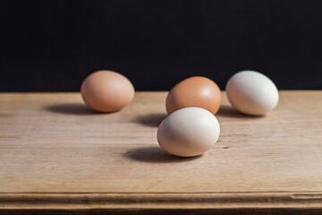 4 eggs of different colors lie on a white oak kitchen board. Close-up photo of food in the studio under artificial lighting.