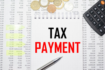 TAX PAYMENT on the block on the background of financial reporting, coins, calculator, pens and yellow stickers. Business concept