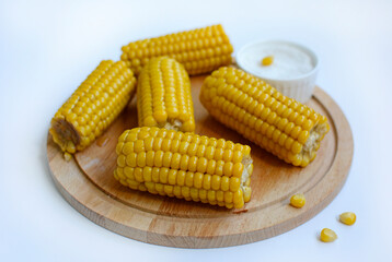 Close-up of juicy yellow corn on a wooden plate on a white background.