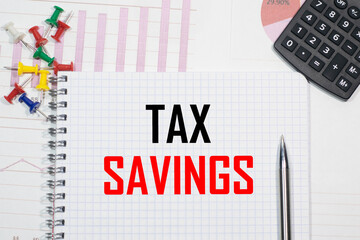 TAX SAVINGS inscription on a notebook against the background of calculator charts, paper clips and pens
