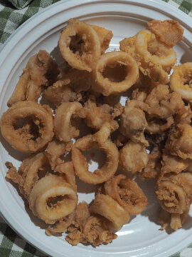 Lunchtime with a typical Italian dish based on fish. Fried squid served as a second dish on a white plastic plate.