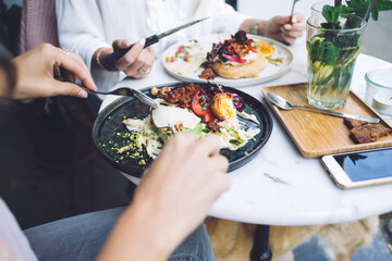 Cropped image of women eating tasty healthy meal with salad and fresh vegetables on lunch break, female having dinner in restaurant enjoying organic vegetarian food dish full of vitamins