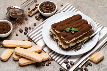 Classic tiramisu dessert and savoiardi cookies on ceramic plate on concrete background
