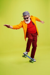 Moving skate. Portrait of senior hipster man in fashionable eyewear isolated on green studio background. Tech and joyful elderly lifestyle concept. Trendy colors, forever youth. Copyspace for your ad.