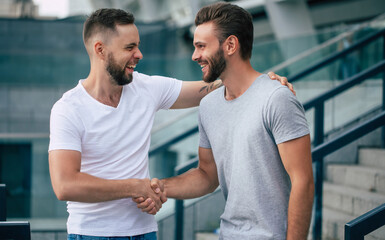 Two happy excited handsome bearded best friends in casual clothes are handshaking, hugging while...