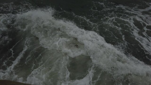 Birds eye view of waves crashing against a sea wall. 4k, 20 seconds.