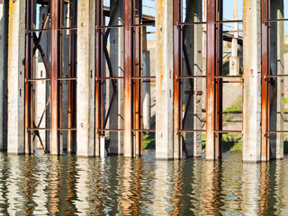 Rusty metal and concrete structures on river. Old abandoned metal structure on stilts in the water in the shallow water.