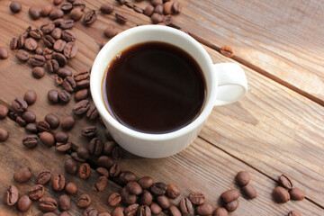 Cup of coffee with beans. Black coffee and scattered coffee beans on wooden table. Selective focus