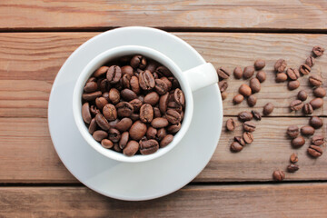 Cup of coffee beans on a wooden table. Close-up of coffee beans in a white ceramic cup on wood background with copy space. Rustic style
