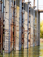 Rusty metal and concrete structures on river. Old abandoned metal structure on stilts in the water in the shallow water.