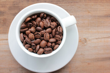 Cup of coffee beans on a wooden table. Close-up of coffee beans in a white ceramic cup on wood background with copy space. Rustic style
