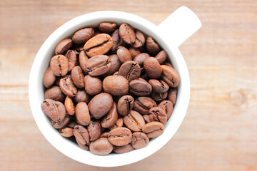 Cup of coffee beans on a wooden table. Close-up of coffee beans in a white ceramic cup on wood background with copy space. Rustic style
