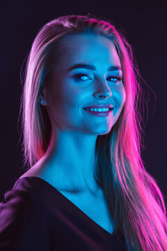 Caucasian woman's portrait isolated on dark studio background in neon light. Beautiful female blonde model with stylish make up. Concept of human emotions, facial expression, sales, beauty, ad