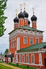 Fototapeta na wymiar red orthodox church with a beautiful white pattern and black domes on a cloudy summer day