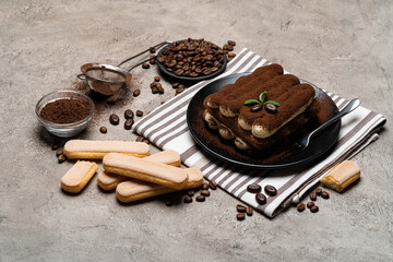 Classic tiramisu dessert and savoiardi cookies on ceramic plate on concrete background