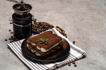 Classic tiramisu dessert and coffee grinder on ceramic plate on concrete background
