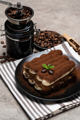 Classic tiramisu dessert and coffee grinder on ceramic plate on concrete background