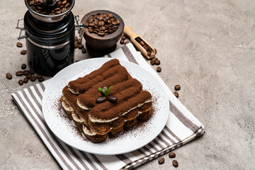 Classic tiramisu dessert and coffee grinder on ceramic plate on concrete background