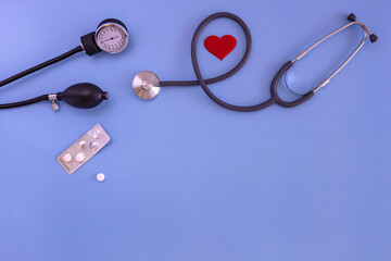 stethoscope, blood pressure cuff, pill, red heart on a blue background. the view from the top