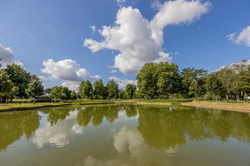 Obraz premium Pond with a mirror reflection in the water surrounded by lush trees in the city park, sunny summer day with a blue sky and white clouds in Sittard, South Limburg, Netherlands