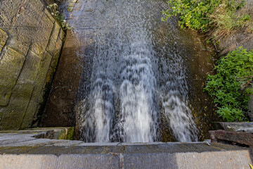 Pressurized water coming out of the weir in the Keutelbeek vita stream from the dam bridge, sunny...