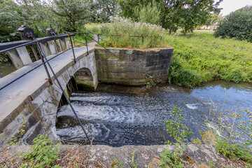 Keutelbeek stream with a small bridge over the dam and sluice with its black metal railing...