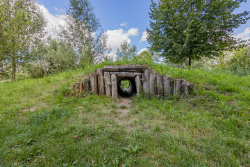 Tunnel between thick wooden logs on a hill with trees and a blue sky in the background in City Play...