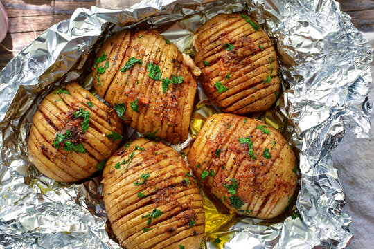 Baked potatoes in foil. Delicious and healthy lunch. Hasselbeck potatoes. Close-up. Wooden background. Top view
