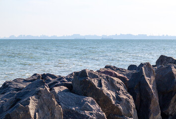 Huge stones of granite on shore of Black sea. Seascape. On horizon in haze of silhouettes of ships and buildings