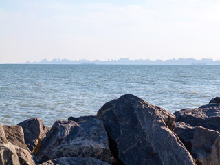 Huge stones of granite on shore of Black sea. Seascape. On horizon in haze of silhouettes of ships and buildings