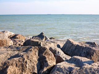 Huge stones of granite on shore of Black sea. Seascape. On horizon in haze of silhouettes of ships and buildings