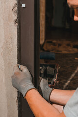 the master installs the front door with a metal box to them, inserts white plugs into the door frame, close-up.