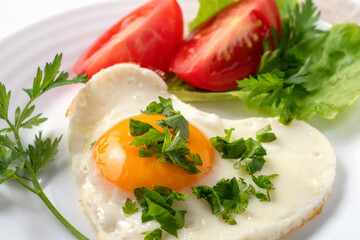Healthy and hearty breakfast. Close-up of a fried eggs, tomato, herbs and espresso coffee. Served on a white table with a linen napkin and cutlery.