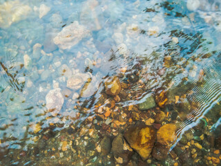 Crystal clear water of river surface with small stones and pebbles.