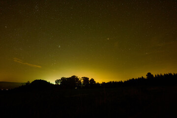 Yellowish night sky with many stars and constellations, the planet Mars can be seen, the forest is shown in silhouette. Germany, Baden-Wuerttemberg.