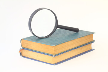 Still-life from a magnifier and a pile of old books on a white background